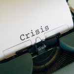 A typewriter with a piece of paper coming out of it that reads "Crisis"
